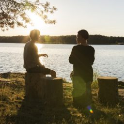 Two people speaking outside by a lake.