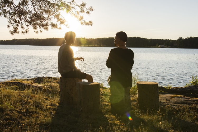 Two people speaking outside by a lake.