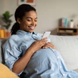 Smiling pregnant woman sitting on the couch looking at her phone.