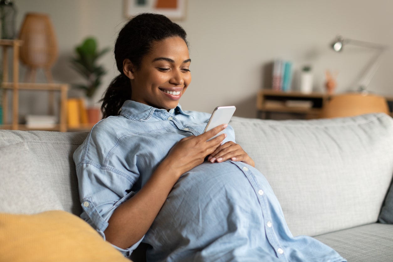 Smiling pregnant woman sitting on the couch looking at her phone.