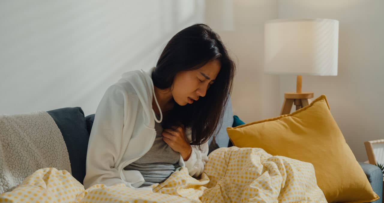 Woman on the couch clutching her chest, experiencing heartburn.