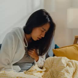 Woman on the couch clutching her chest, experiencing heartburn